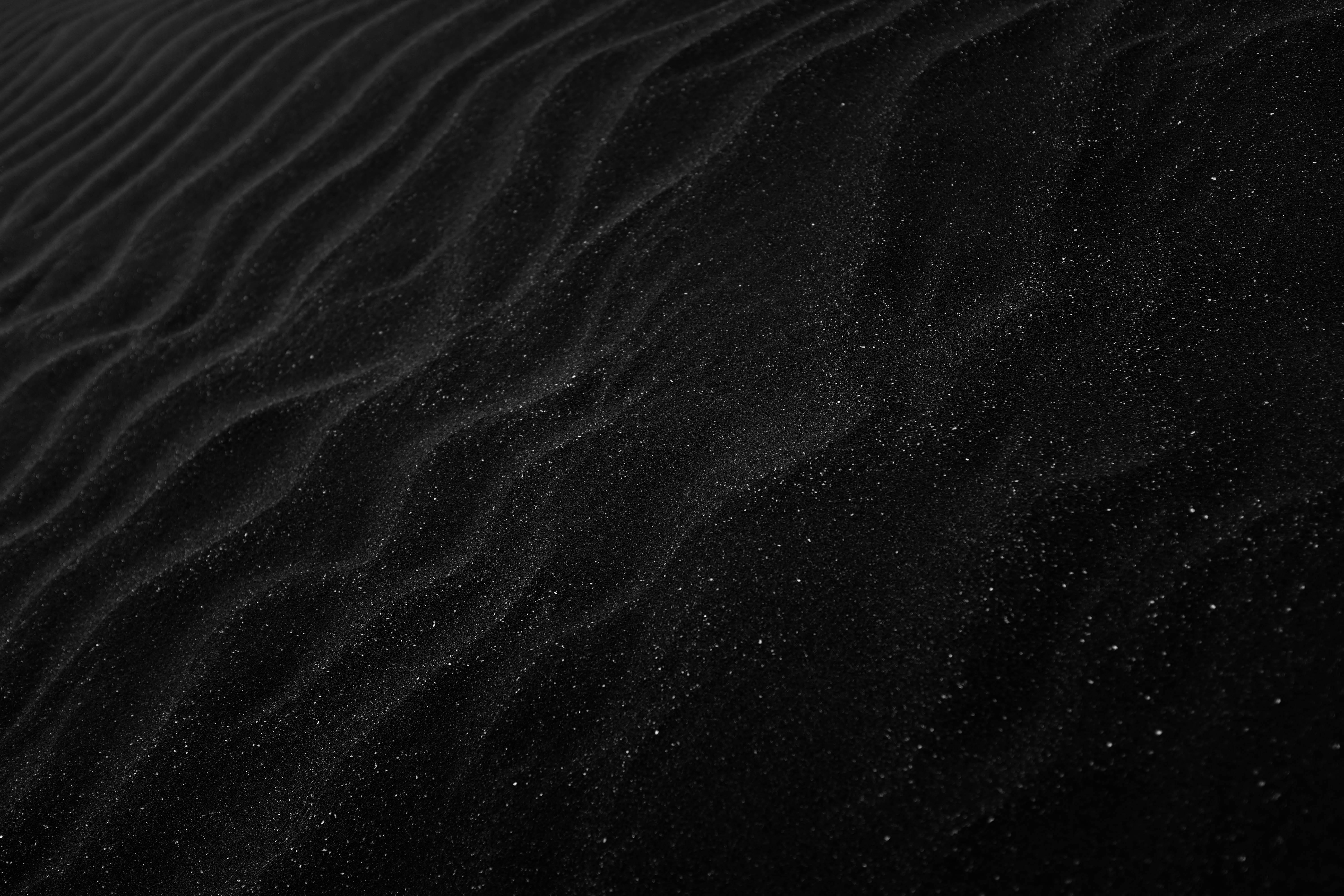 Textured black sand with ripples resembling dunes, creating a dark, abstract aesthetic.